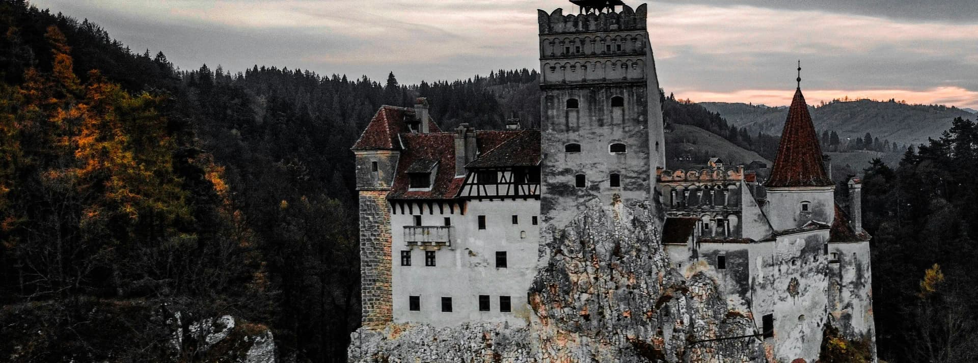 Bran Castle at dusk on its rock above the forest, Transylvania, Romania.
